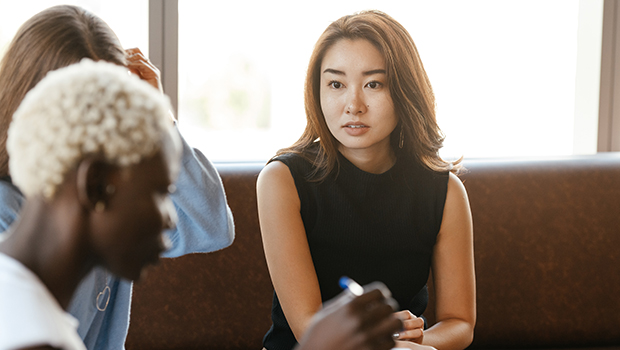 A woman is sat on a leather back sofa. She is looking over at her colleague who is sitting to the left of her.