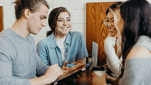4 people are sat facing each other and engaged in conversation. They are sat in a wooden booth with a bricked wall.