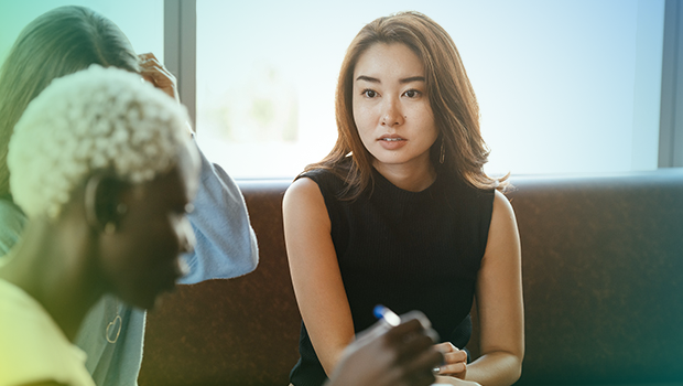A woman is sat on a leather back sofa. She is looking over at her colleague who is sitting to the left of her.