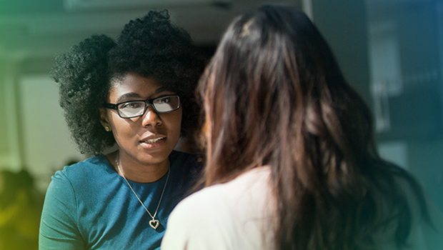 A woman is sat across from another woman at a small round table. They are having a conversation.