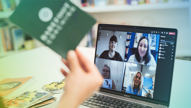 4 people are talking to a woman on a teams call. The women is holding coaching flash cards to the screen.