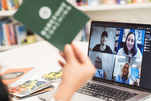 4 people are talking to a woman on a teams call. The women is holding coaching flash cards to the screen.
