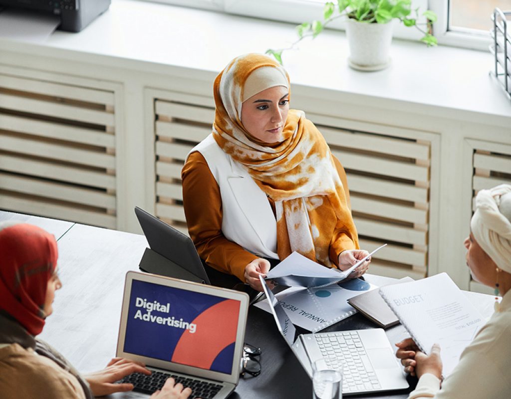 3 woman are looking over a digital advertising presentation. They are also looking thorough documents.